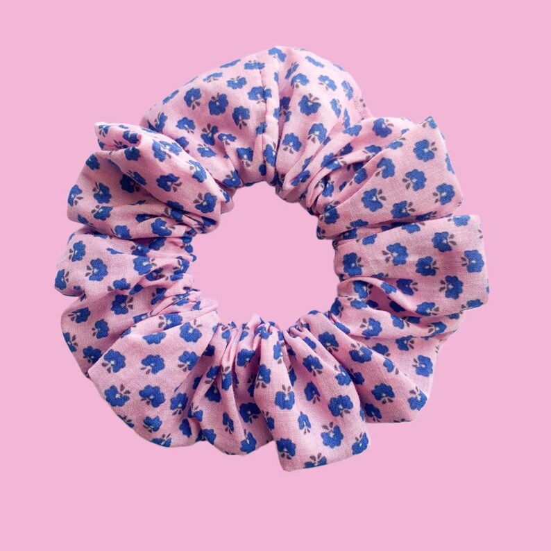 May include: A pink and blue floral scrunchie made of fabric. The scrunchie is gathered and tied into a circle.
