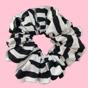 May include: A black and white striped scrunchie made of fabric. The scrunchie is gathered and tied into a circle.