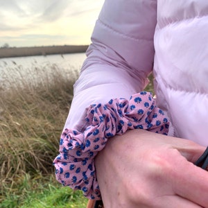 May include: A pink puffer jacket with a floral print scrunchie on the sleeve.