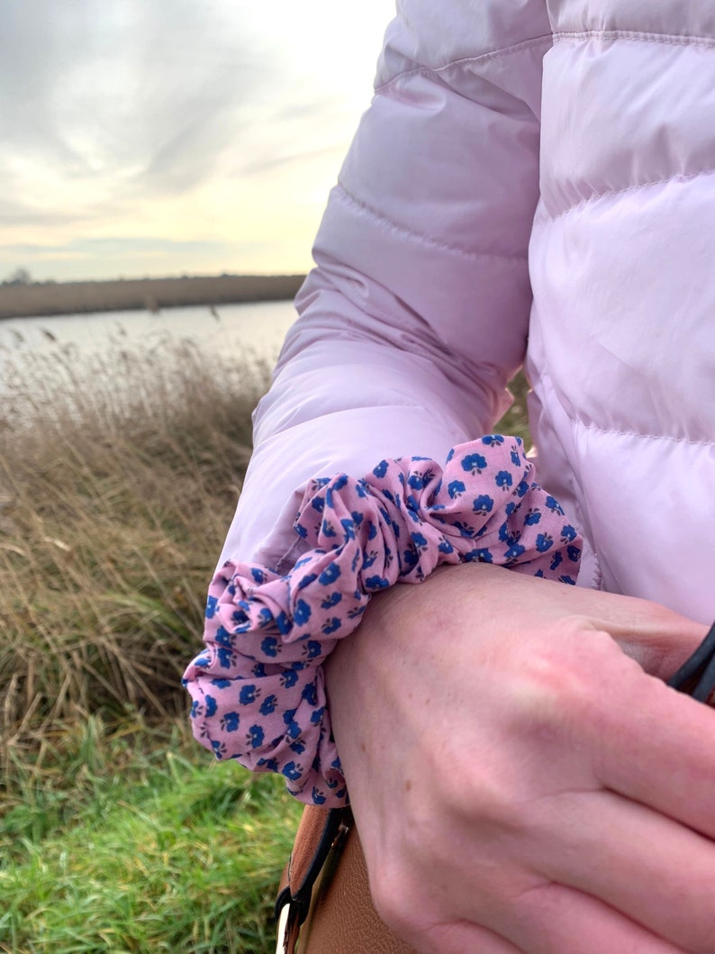 May include: A pink puffer jacket with a floral print scrunchie on the sleeve.