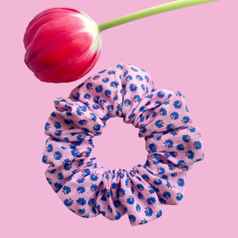 May include: A pink and blue floral patterned scrunchie. The scrunchie is made of fabric and has a gathered look.