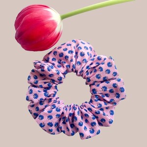 May include: A pink scrunchie with a blue floral pattern. The scrunchie is made of fabric and is tied in a knot.