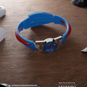 Puede incluir: Una pulsera azul y roja con un emblema plateado. La pulsera tiene un diseño curvo con detalles en rojo y un emblema central. La imagen también incluye texto: "Archivos digitales para impresión 3D" y "ABYSSMO WORKSHOP".