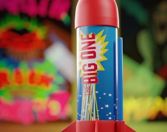 May include: A toy rocket with a red cone and fins, a blue body with the text "THE BIG ONE" in a yellow burst, and white stars. The rocket is standing upright.