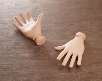 May include: Two detached, light-toned, open-palmed hand sculptures with a cylindrical base. The hands are positioned on a brown, wood-grain surface. The sculptures appear to be made of a smooth, matte material.