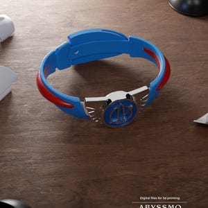 Könnte beinhalten: Ein blau-rotes, kreisförmiges Armband mit einem zentralen, metallisch silbernen Emblem in kreisförmigem Design. Das Armband hat eine glatte Oberfläche und enthält unten rechts den Text Digital files for 3d printing ABYSSMO WORKSHOP.