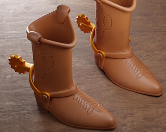 Puede incluir: Dos botas vaqueras de color marrón claro con espuelas doradas en los talones. Cada bota presenta un diseño de cactus cosido en la caña y un patrón decorativo en la punta. El texto en la parte inferior dice: Digital files for 3d printing ABYSSMO WORKSHOP.