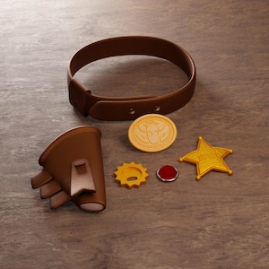 Könnte beinhalten: Auf einer Holzoberfläche liegen ein brauner Ledergürtel, ein Handschuh, ein goldener Sheriffstern, eine goldene Münze mit Bullenmuster, ein gelbes Zahnrad und ein roter Edelstein. Die Gegenstände gehören wahrscheinlich zu einem Kostüm- oder Spielzeugset.