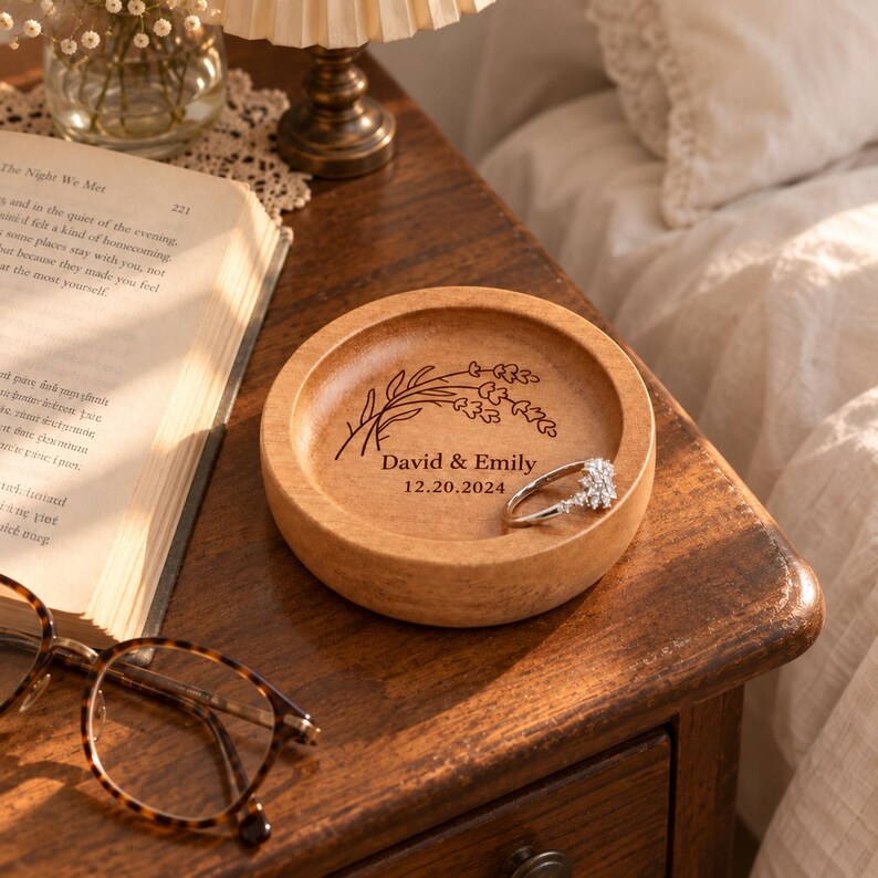 May include: A round wooden trinket dish featuring a laser-engraved lavender sprig, the names David & Emily, and the date 20.12.2024. A silver-toned ring with clear stones rests inside the bowl, which has a smooth, light brown wood grain finish.