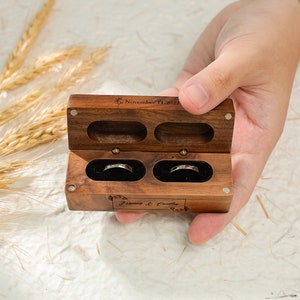 May include: A wooden ring box with two compartments for rings. The box is engraved with the date "November 11, 2022" and the names "Francis & Coralie".