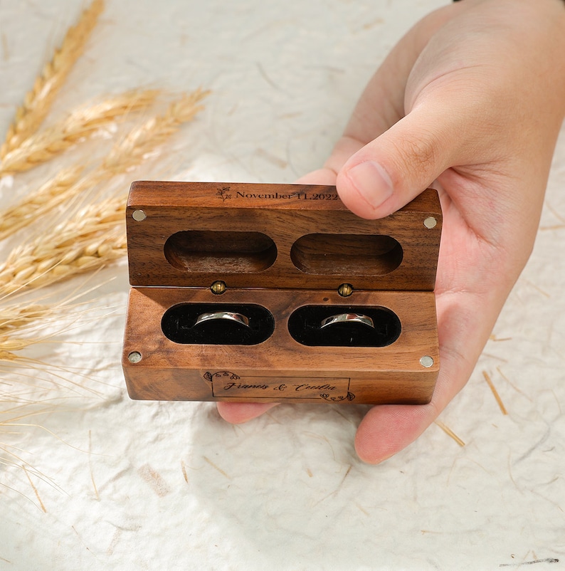 May include: A wooden ring box with two compartments for rings. The box is engraved with the date "November 11, 2022" and the names "Francis & Coralie".