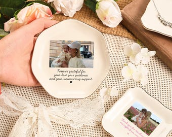 May include: Off-white ceramic trinket dish with a gold rim, featuring a photograph and the text "Forever grateful for your love, your guidance, and your unwavering support." Additional dishes and flowers are in the background.
