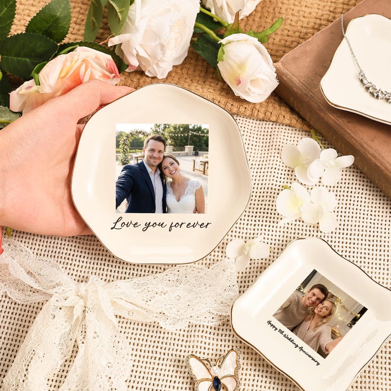 Puede incluir: Plato de cer&aacute;mica blanquecina con borde dorado, con una foto de una pareja y el texto "Love you forever". El plato est&aacute; sostenido por una mano, rodeado de flores y otros objetos decorativos. Se ve un segundo plato.