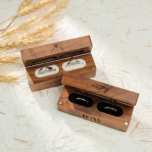 May include: Two wooden ring boxes with engraved details. The top box has a ring design and the text "Crystal" engraved on the side. The bottom box has a floral design and the text "R-W 02.11.2023" engraved on the bottom.