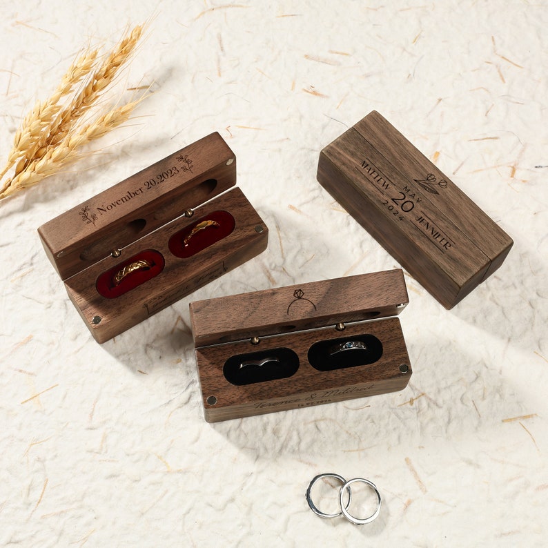 May include: Two wooden ring boxes with engraved dates and names. One box is open and shows two silver rings inside. The other box is closed and has a red velvet interior.
