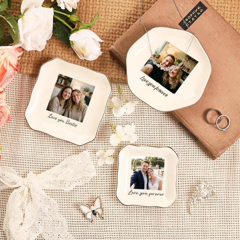 Puede incluir: Tres platos decorativos de cer&aacute;mica con fotos y texto. Los platos tienen una base blanca con un borde plateado. El texto en los platos dice "Love you Bestie" y "Love you forever". La imagen tambi&eacute;n incluye un broche de mariposa, anillos y flores.
