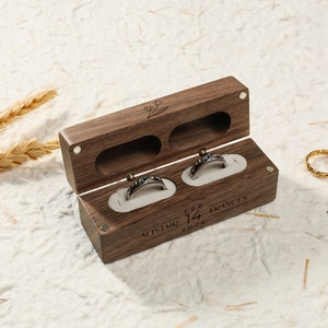 May include: A wooden ring box with two compartments for rings. The box is engraved with the names "Alistair" and "Frances", the date "Feb 14, 2024", and a small floral design.