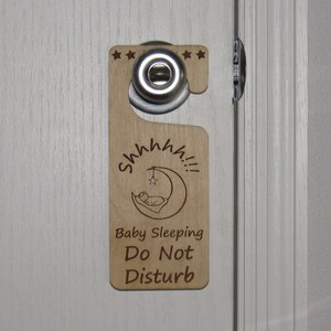 May include: Wooden door hanger with a crescent moon and a sleeping baby design. The text reads "Shhh... Baby Sleeping Do Not Disturb".