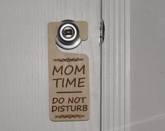 May include: A wooden door hanger with the text "MOM TIME DO NOT DISTURB" in brown lettering. The hanger has a silver hook and a decorative design.