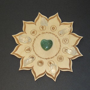 May include: A wooden lotus flower-shaped tray with a green heart-shaped stone in the center. The tray has symbols representing different religions and the text "May the followers of all religions and spiritual paths work together to create peace among all the people of earth."
