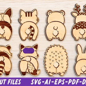 May include: A collection of eight laser-cut wooden animal rear-view ornaments featuring a dog, cat, bear, deer, raccoon, fox with a purple mask, hedgehog, and rabbit, each with a small white pom-pom tail attached to the centre of the design.