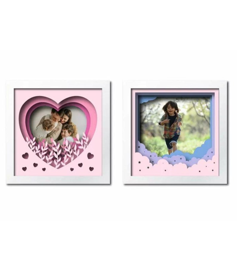 Peut inclure: Deux cadres photo blancs avec un design en papier d&eacute;coup&eacute; en 3D. Le cadre de gauche a un c&oelig;ur rose avec une photo de famille &agrave; l'int&eacute;rieur. Le cadre de droite a un design de nuage bleu et rose avec une photo d'un enfant courant dans un champ.