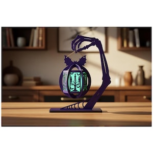 May include: A dark purple decorative stand shaped like a skeletal arm and hand holding a hanging lantern. The lantern features a bat-shaped top and cut-out designs of trees and candles, illuminated from within by a soft, glowing light.