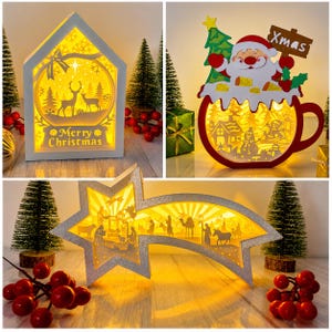 Puede incluir: Un conjunto de tres decoraciones navideñas iluminadas: un marco blanco en forma de casa con la silueta de un ciervo y el texto Merry Christmas, un marco rojo en forma de taza con Santa Claus y un muñeco de nieve, y un pesebre en forma de estrella plateada.