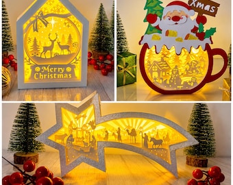 Op de afbeelding: Een set van drie verlichte kerstdecoraties: een wit huisvormig frame met een hert-silhouet en de tekst Merry Christmas, een rood mokvormig frame met de Kerstman en een sneeuwpop, en een zilverkleurige, stervormige kerststal-display.