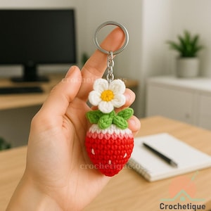 Può includere: Un portachiavi a forma di fragola all'uncinetto fatto a mano, con un fiore bianco e foglie verdi. La fragola rossa ha dettagli di semi bianchi ed è attaccata a un portachiavi argentato. Un accessorio affascinante.