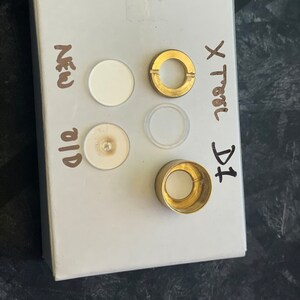 以下が含まれることがあります： 白いカードに、左側に「New」と「Old」が縦に書かれています。右側に「X Trail DCI」が縦に書かれています。カードには、白い円が2つ、透明な円が1つ、金色の円が1つの合計4つの丸い物体が置かれています。