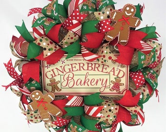 May include: A Christmas wreath decorated with red, green, and brown ribbon, gingerbread men, and a sign that reads "Made Fresh With Love Gingerbread Bakery".