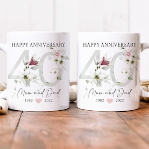 May include: Two white ceramic mugs with a floral design and the number 40. The mugs say "Happy Anniversary" and "Mum and Dad 1982 2022".