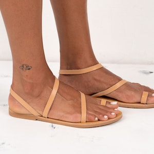 May include: Tan leather sandals with a toe ring and ankle strap. The sandals have a flat sole and are made of a soft, supple leather.