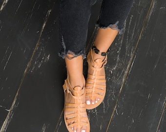 May include: A pair of tan leather gladiator sandals with ankle straps. The sandals have a woven design and are worn on a person's feet.