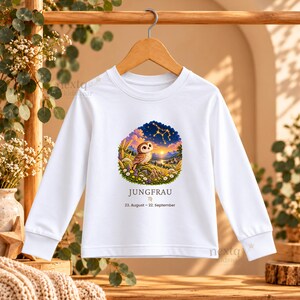 May include: A white long-sleeve shirt featuring a graphic of an owl perched in a field with a sunset and constellation background. Below the graphic, the text reads JUNGFRAU, the Virgo symbol, and the date range 23. August &ndash; 22. September.