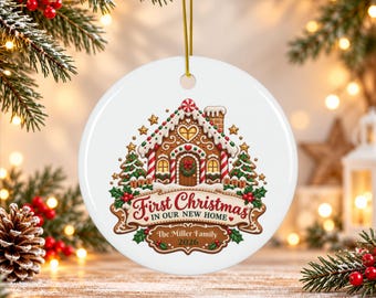May include: A round white ceramic ornament featuring a gingerbread house illustration with icing details, two pine trees, and a banner with the text "First Christmas IN OUR NEW HOME" and "The Miller Family 2026" in red and brown script.