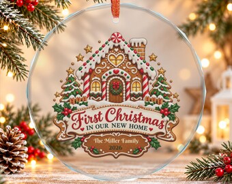 May include: A round, clear glass ornament with a red ribbon hanger featuring a gingerbread house illustration, green pine trees, and red holly berries. The text reads First Christmas IN OUR NEW HOME, The Miller Family, and 2026.