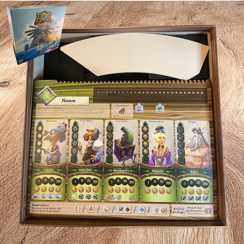 May include: A board game box containing a game board with the title Noom, featuring five character cards with illustrations of fantasy figures, a numbered track from 0 to 25, and various icons. A separate game box lid is shown in the top left corner.