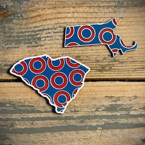 May include: Two state-shaped wooden cutouts with a red and blue circle pattern. The cutouts are of the states of Massachusetts and South Carolina.