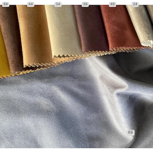 May include: A selection of fabric swatches in various colors, including yellow, brown, and burgundy. The swatches have a textured appearance and are arranged in a row. A large piece of blue fabric is in the foreground, with the number 66 in the corner.