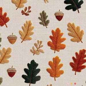 Op de afbeelding: Een stof met een herhalend patroon van geborduurde herfstbladeren en eikels. De bladeren zijn in tinten oranje, geel en groen, terwijl de eikels bruine doppen hebben. De achtergrond is een lichtbeige stof.