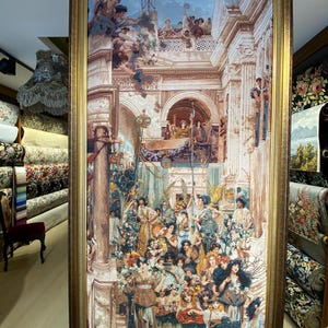 Puede incluir: Un tapiz enmarcado que representa una escena clásica con numerosas figuras con ropa ornamentada. La obra de arte presenta un detallado fondo arquitectónico con columnas y arcos, y está encerrada en un marco dorado. El tapiz se exhibe en un entorno comercial.