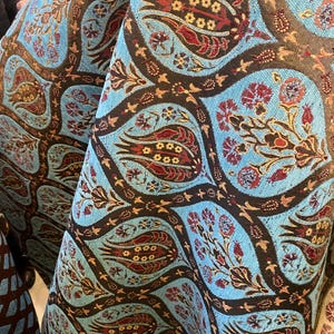 Puede incluir: Primer plano de una tela con un patrón repetido de flores y hojas estilizadas en tonos turquesa, marrón y burdeos. El diseño tiene un aspecto tradicional y ornamentado, adecuado para tapicería o textiles decorativos.