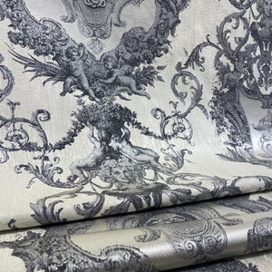 Puede incluir: Tela color crema con un patrón repetido de figuras clásicas, querubines y adornos ornamentados en tonos grises y negros. El diseño tiene una estética vintage y barroca, adecuada para tapicería o proyectos decorativos.