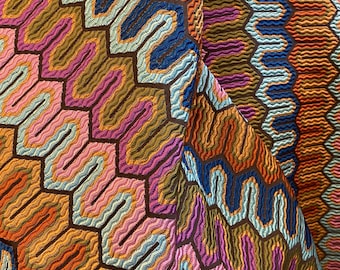 Puede incluir: Primer plano de una tela colorida con un diseño geométrico. El diseño presenta una estructura repetitiva en forma de panal con líneas onduladas en tonos naranja, azul, rosa y marrón. La tela tiene una apariencia texturizada.