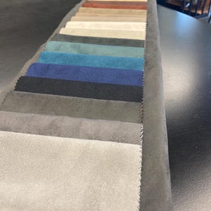 May include: A fabric swatch book displaying a variety of colors. The swatches range from light beige to dark navy and black, with shades of blue, green, and brown in between. The samples are arranged in a neat, organized row.