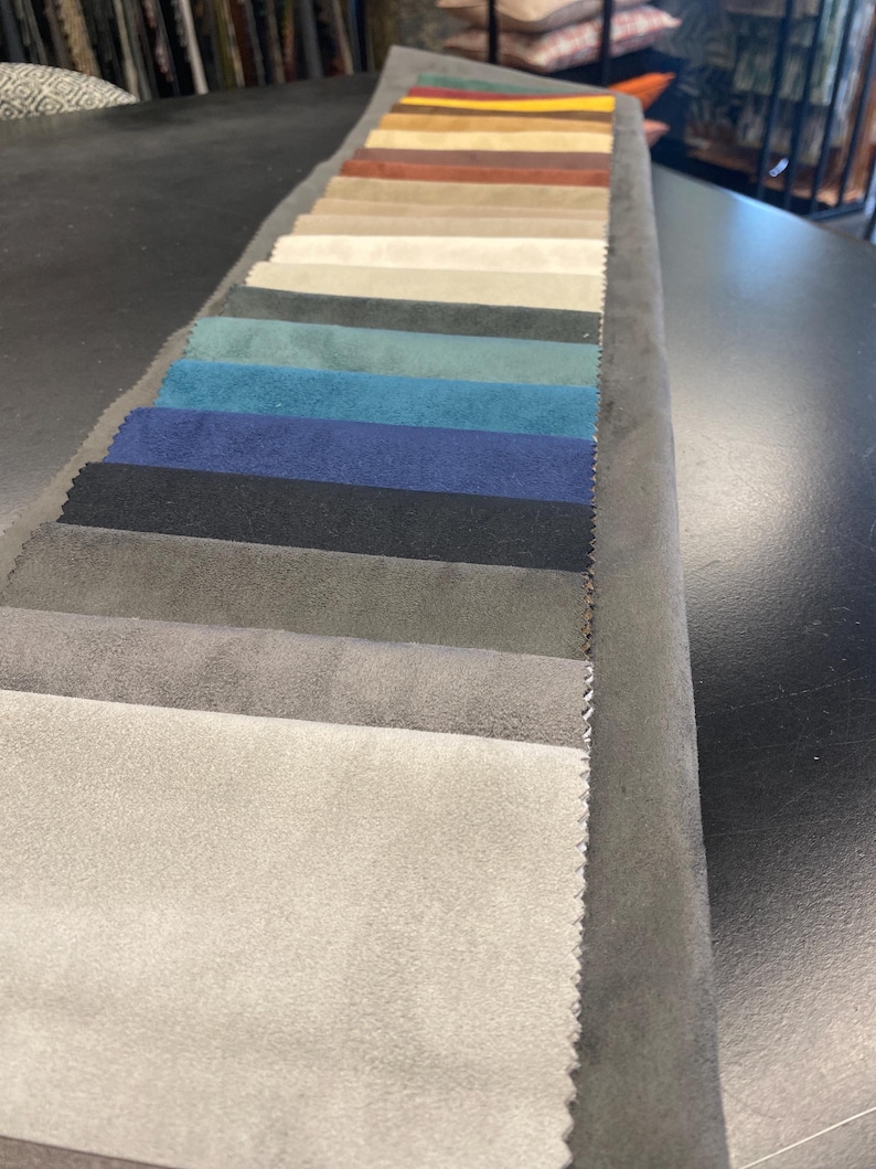 May include: A fabric swatch book displaying a variety of colors. The swatches range from light beige to dark navy and black, with shades of blue, green, and brown in between. The samples are arranged in a neat, organized row.