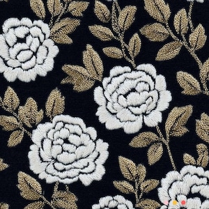 Op de afbeelding: Close-up van een zwarte stof met een geborduurd bloemenpatroon. Witte bloemen met gedetailleerde steken worden afgewisseld met goudkleurige bladeren en stelen. Het ontwerp herhaalt zich over de stof.