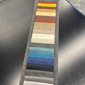 May include: A fabric swatch card featuring a variety of colors. The card displays rectangular fabric samples in shades of green, red, yellow, brown, beige, blue, and gray. The samples are arranged vertically on a gray backing.